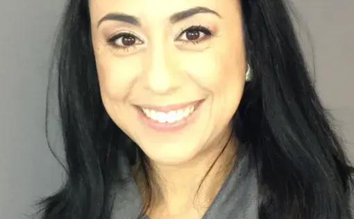A woman wearing a grey shirt smiles at the camera.
