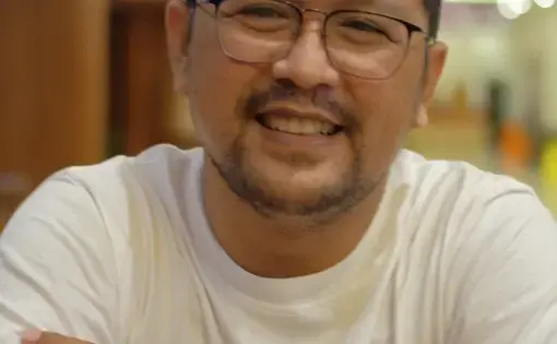 A man with glasses smiles into the camera.