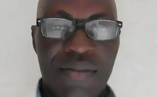 A man wears glasses and a white shirt, he smiles at the camera.