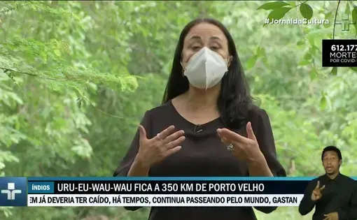 A woman talks as she wears a black shirt and a medical mask.