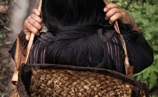 A woman carries a brown bag on her shoulders.
