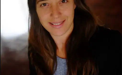 A woman wears a black jacket and blue blouse.