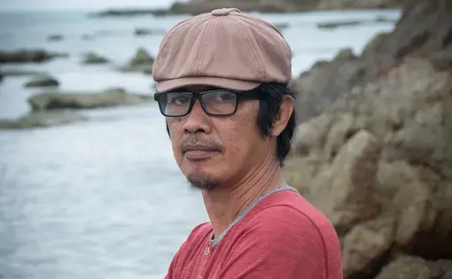A person wears glasses, a brown baseball cap, and a red shirt.