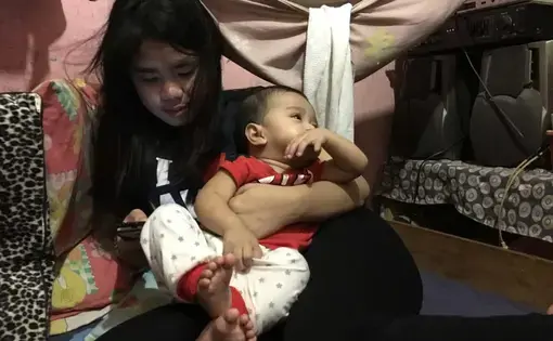 Young girl holds baby while texting