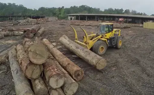 A person drives a tractor and uses it to pick up wood logs.