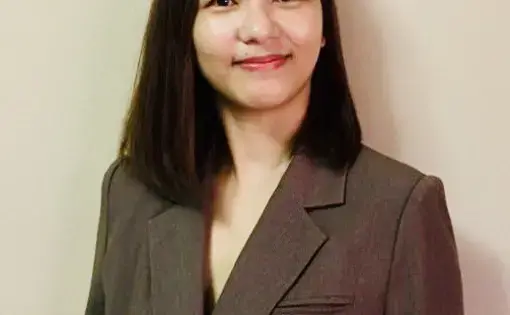 A person wears a brown jacket and has shoulder length black hair.