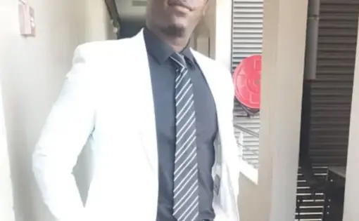 A man wears a white jacket and dark blue shirt with a striped tie.