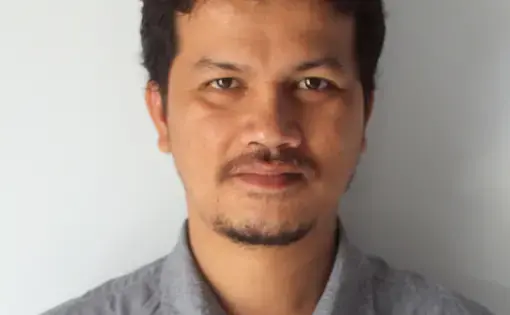 A person wears a grey shirt and has short black hair.