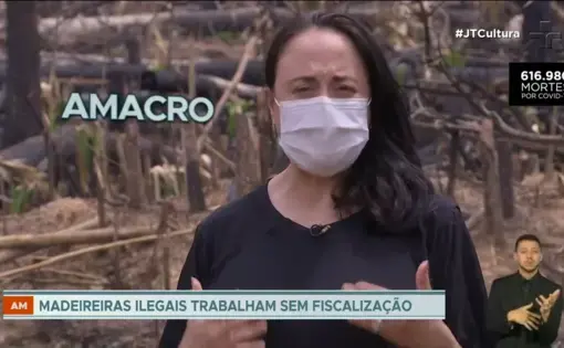 A person talks with a medical mask on, in the foreground is a series of deforested trees.