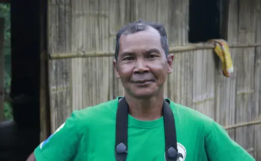 A person wears a green shirt and a camera strap.
