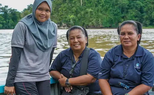 Three people are wearing blue shirts with black sleeves and black pants. They are riding a boat.