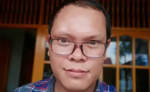 A person wears a blue shirt with glasses.