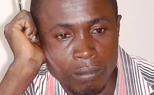 A person wears a red and white patterned shirt. The person is also holding a pen.