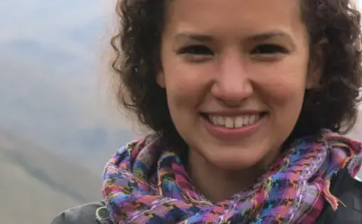 A woman with curly hair and a purple scarf stares in the camera