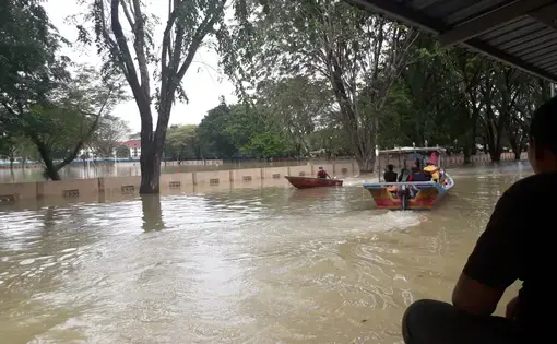 A person sits inside a restaurant. Outside, there is a flood and a boat carrying people.
