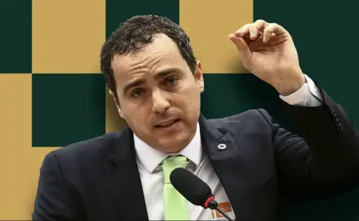 A person wears a black suit with a white shirt and green tie. He is talking and using a hand gesture.