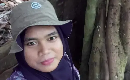 A person wears a cap, purple shirt, and a purple scarf.