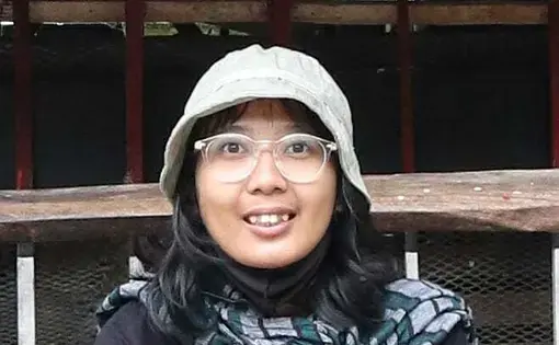 A person wears a cap and glasses. She is also wearing a black long sleeve shirt.