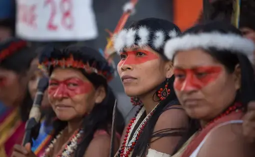 Three Indigenous women wear headdresses and ceremonial outfits during a protest.