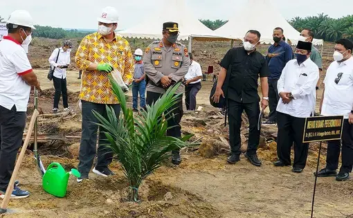 A person digs the soil with a shovel as five other people watch him.
