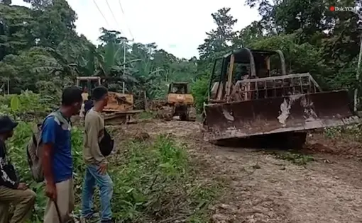 Three people look as tractors and excavators driven down a muddy road.