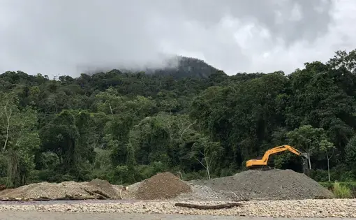 A excavator machine is on top of a pile of rocks and sand.