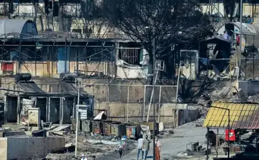 view of people walking down a street with burned metal structures and trees
