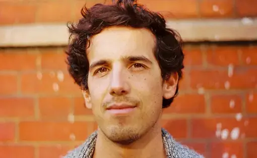 A person has curly brown hair and wears a grey jacket.