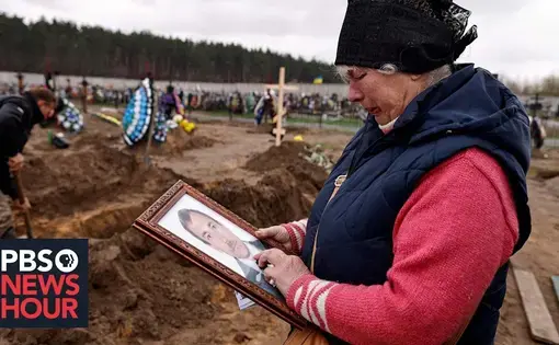 a woman looks at a photograph in a graveyard where earth has recently been undug