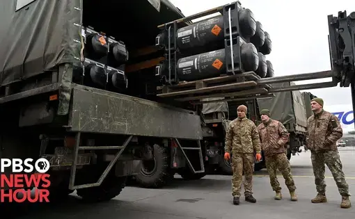 soldiers stand below trucks loaded with large rockets