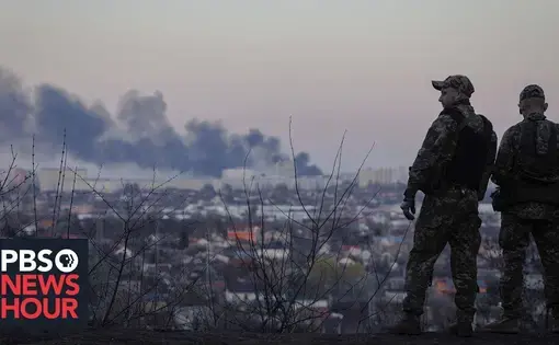 two uniformed men look over a city while a building burns in the background