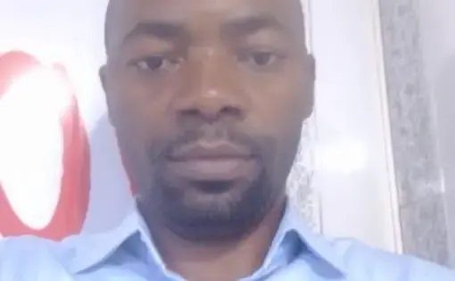 A bald man wears a light blue workshirt.