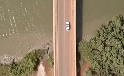 a car goes over a bridge. the earth on one bank is rusty orange, and the water is green.