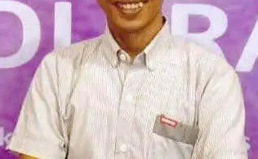 A man wears a grey shirt and an Indonesian, black songkok hat.
