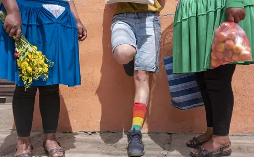 a person wearing shorts and rainbow socks stands between two people wearing pollera skirts