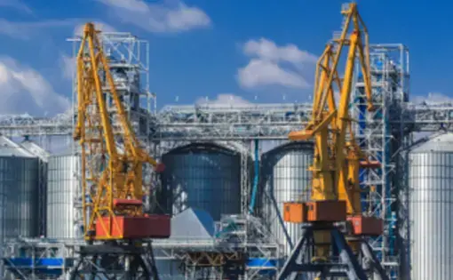 large yellow cranes sit on the water next to huge grain silos