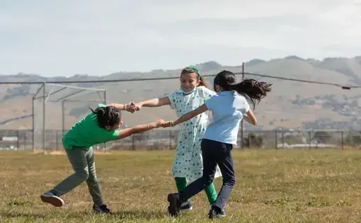 children play in a field holding hands in a circle
