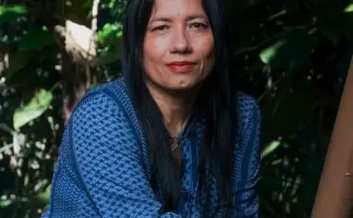 A woman wears a blue-striped shirt with a bracelet. She has black hair and looks at the camera.