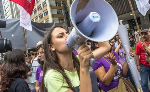 a woman surrounded by protesters and flags shouts through a megaphone