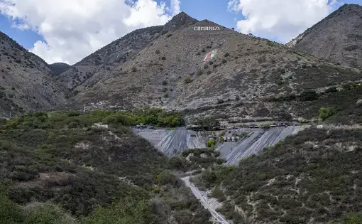 A mine at the base of a mountainscape. 'Carmago' is emblazoned on the center peak.