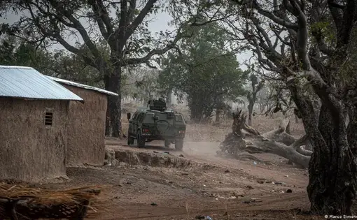 A military Humvee kicks up dust along a village road.