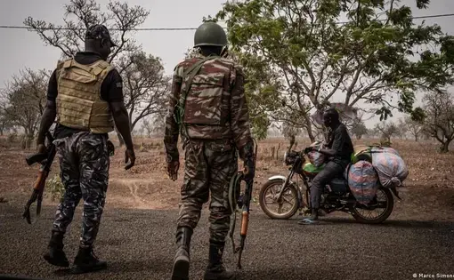 Two soldiers carrying automatic rifles stop a man on a motorbike.