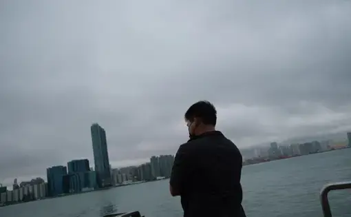 A man looks out on a city skyline bordered by water and milky sky.