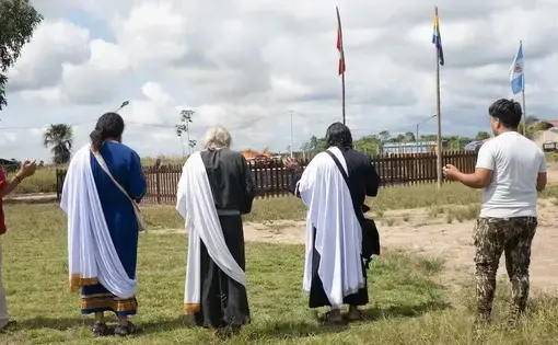 four men in religious robes stand in a field facing away towards three flag posts
