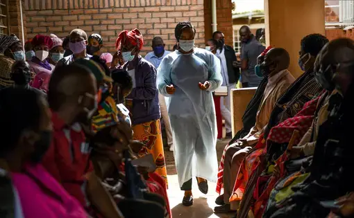 A health worker walks through a crowded clinic in Malawi. Citizens waiting for their appointments look on.