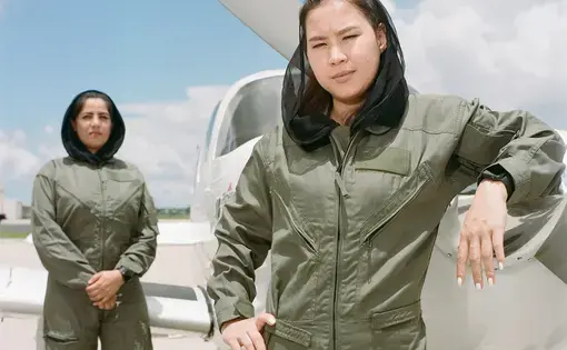 two young women in veils and air force uniforms pose near a small aircraft