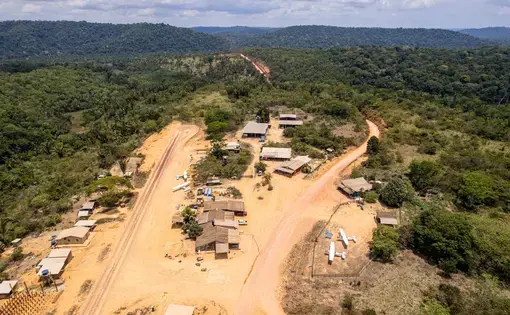 aerial view of a small settlement set around a dirt airstrip in the middle of thick vegetation