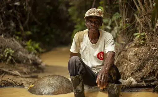 A man sits by the river where he pans for gold.