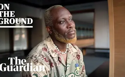 A Black man looks pensively away from the camera. Thumbnail from "I count myself as a Black Ukrainian: the fashion designer starting again in Budapest" video. Over the photo reads "On the Ground" and "The Guardian"