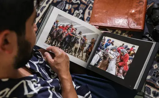 a photographer sits and flips through a photo album with two pictures of groups of men wearing helmets on horses in a sport similar to polo